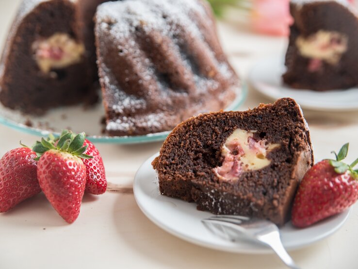 Mit Käsekuchen gefüllter Schokokuchen mit Erdbeeren auf weißem Teller. 