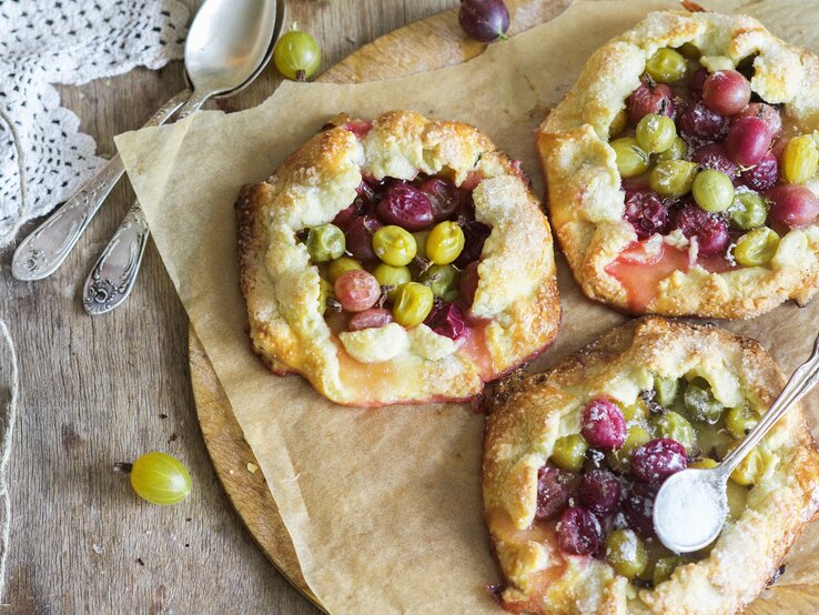 Mini-Stachelbeer-Pies Drei kleine Stachelbeerkuchen auf einem Blech mit Backpapier direkt von oben fotografiert.