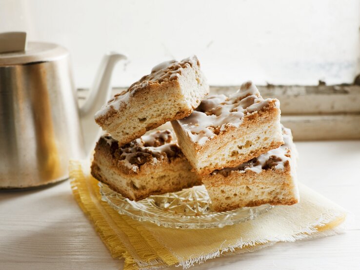 Mehrere Kuchenstücke auf einem hellen Kaffeetisch mit Kanne im Hintergrund.