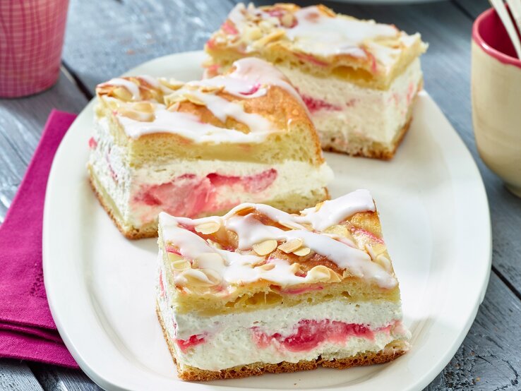 Auf einem ovalen hellen Teller aus Porzellan sind drei Stücke Rhabarber-Kuchen