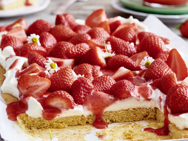 Der angeschnittene Erdbeer-Kuchen in der Nahaufnahmen mit Frühlingsblumen. 