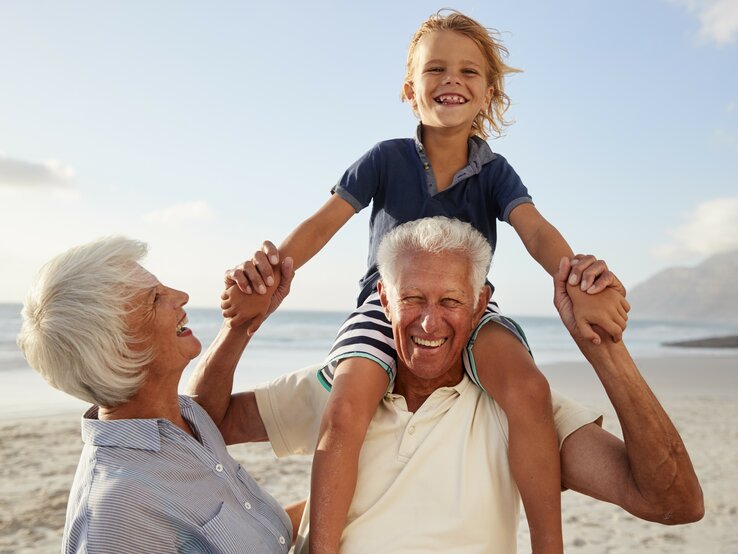 Großeltern mit Enkelkind am Strand. Kind sitzt beim Opa auf den Schultern