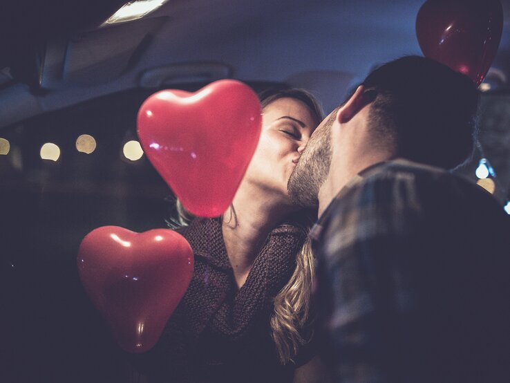 Ein verliebtes Paar küsst sich und hält dabei Herz-Luftballons in den Händen | © iStock/mixetto