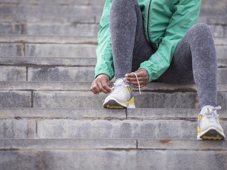 Frau bindet sich die Schuhe zu. | © iStock / RuslanDashinsky