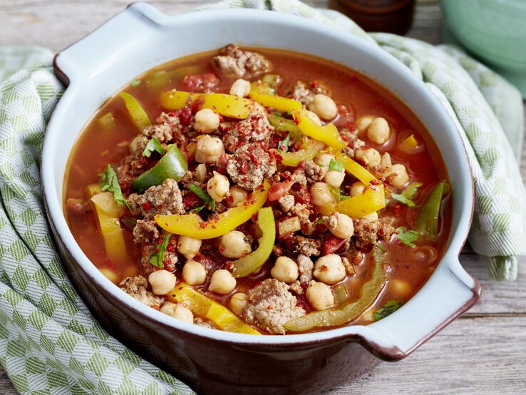 Orientalischer Kichererbseneintopf mit Paprika, Chili, Hackfleisch und Kichererbsen in einer hellen Form auf einem Holztisch