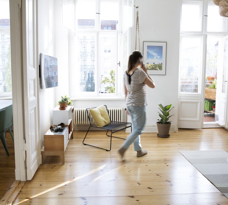 Frau läuft mit Telefon am Ohr in der Wohnung umher. | © Getty Images/Westend61