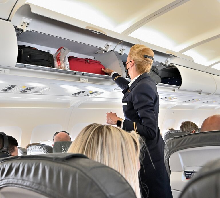 Eine Flugbegleiterin vor einem geöffneten Gepäckfach mit Handgepäck. | © IMAGO / Rolf Poss