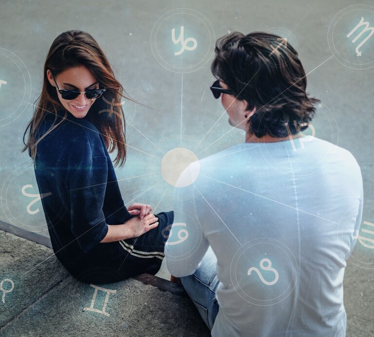Von oben blickt man auf ein Paar, das auf einer Bank sitzt. Beide schauen aneinander vorbei. Darum herum die astrologischen Symbole der Tierkreiszeichen. | © Shutterstock [M]