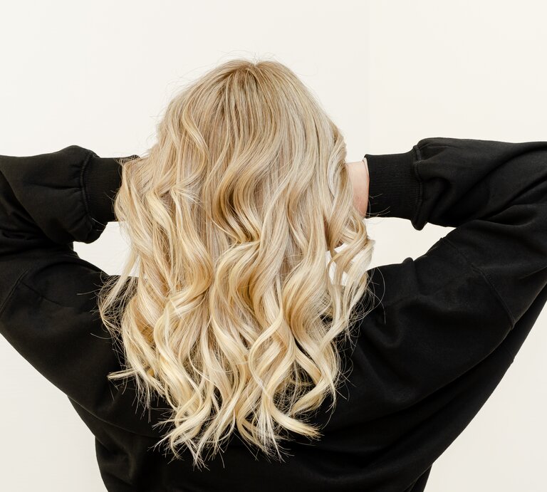 Eine Frau mit blonden Haaren steht mit dem Rücken zur Kamera und fasst in ihre Haare. Sie trägt ein schwarzes Oberteil. | © Getty Images/ Serhii Tychynskyi