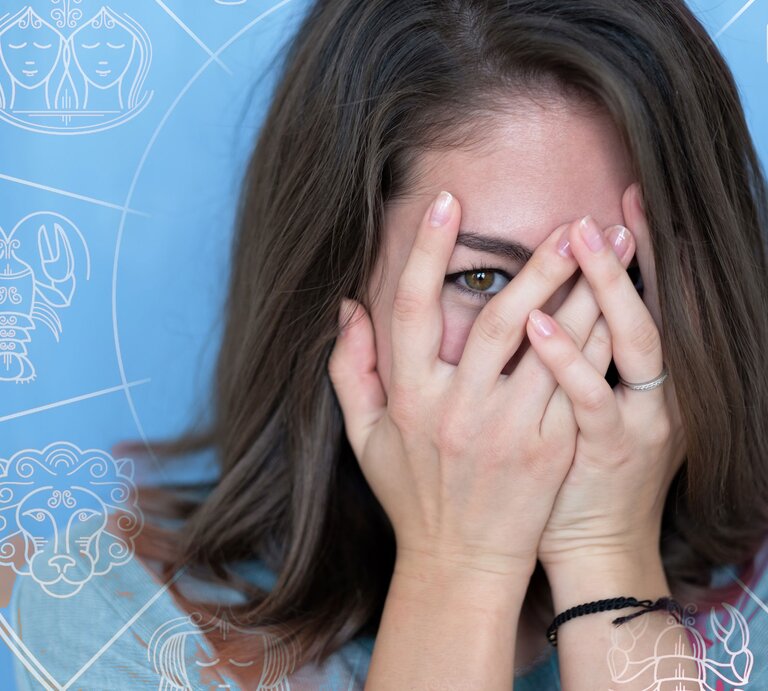 Frau schämt sich und versteckt sich hinter Händen mit Sternkreissymbolen | © iStock, Shutterstock [M]