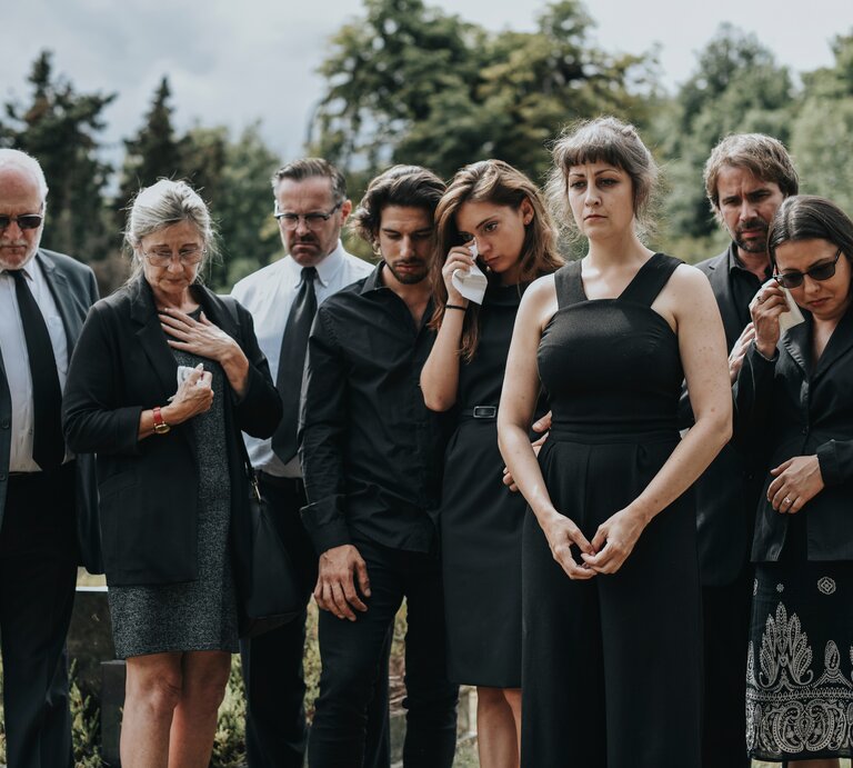 Personen in schicker Kleidung stehen an einem Grab und trauern. | © Shutterstock/Rawpixel.com