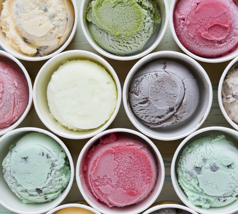 Mehrere bunte Sorten Eis in Pappbechern direkt von oben fotografiert. | © iStock/Tatomm 
