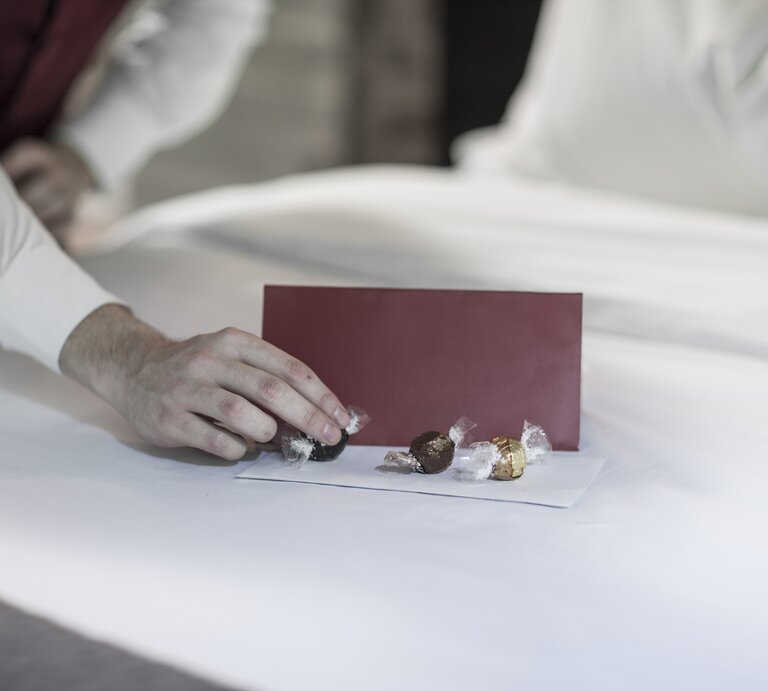 Eine Person legt Pralinen auf das Hotelbett. | © Getty Images / Westend61