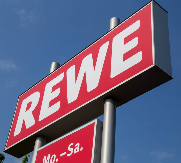 Das Rewe-Logo vor dem blauen Himmel | © IMAGO / Herrmann Agenturfotografie