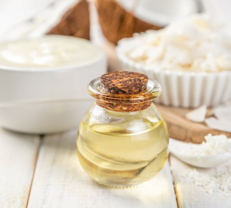 MCT-Öl wird aus Kokos- oder Palmkernöl hergestellt. Die darin enthaltenen Fettsäuren sollen leistungsfähig und schlank machen. Eine Flasche mit Öl ist im Vordergrund zu sehen. | © iStock.com/a_namenko