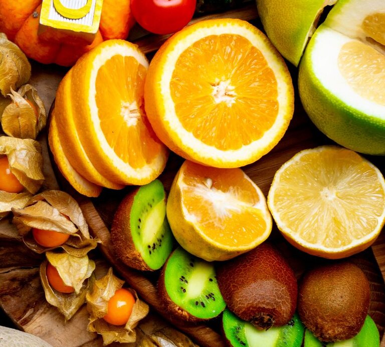 Aufgeschnittene Orangen, Grapefruit, Kiwi und Physalis liegen nebeneinander auf einem Holzuntergrund und zeigen eine Auswahl vitamin-C-reicher Früchte. | © Getty Images/ Artemidovna von Canva.com 