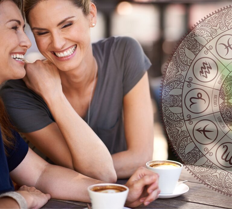 Ein fröhliches Bild zeigt zwei Frauen mittleren Alters, die lachend an einem Außentisch sitzen und Kaffee trinken. Die eine Frau mit braunem Haar flüstert der anderen, einer Frau mit blondem Haar, etwas ins Ohr, was beide zum Lachen bringt. Im Hintergrund ist ein halbtransparentes, großes Mandala mit astrologischen Symbolen zu sehen, was eine entspannte und freundliche Atmosphäre unterstreicht. | © iStock [M]
