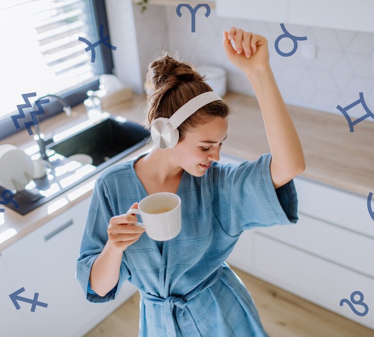 Eine junge Frau in einem entspannten blauen Kleid mit weißen Kopfhörern tanzt in einer hellen Küche und hält eine Tasse Kaffee. Sie scheint glücklich und energiegeladen zu sein. Über das Bild verteilt sind verschiedene Astrologie-Symbole wie Zwillinge, Wassermann, Steinbock und Krebs, die darauf hindeuten könnten, dass das Bild sich mit Astrologie oder Horoskopen beschäftigt. | © Adobe Stock/ Halfpoint und Chikovnaya via Canva.com [M]