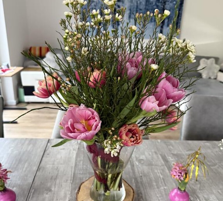 Ein bunter Frühlingsstrauß mit rosa Tulpen und kleinen weißen Blüten steht in einer Vase auf grauem Holztisch. | © Madeleine Liedke 