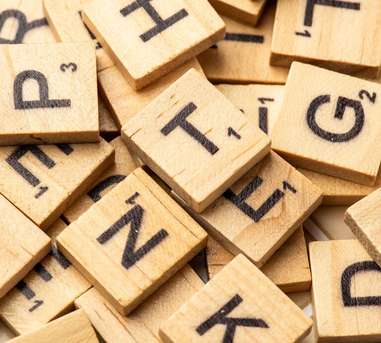 Ein Haufen hölzerner Scrabble-Buchstabensteine mit schwarzen Lettern liegt chaotisch durcheinander. | © Adobe Stock/Adriana