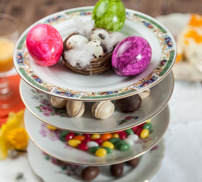 Eine elegante Etagere aus verzierten Porzellantellern mit Ostereiern, Pralinen, Macarons und bunten Süßigkeiten. | © Adobe Stock/Lilli
