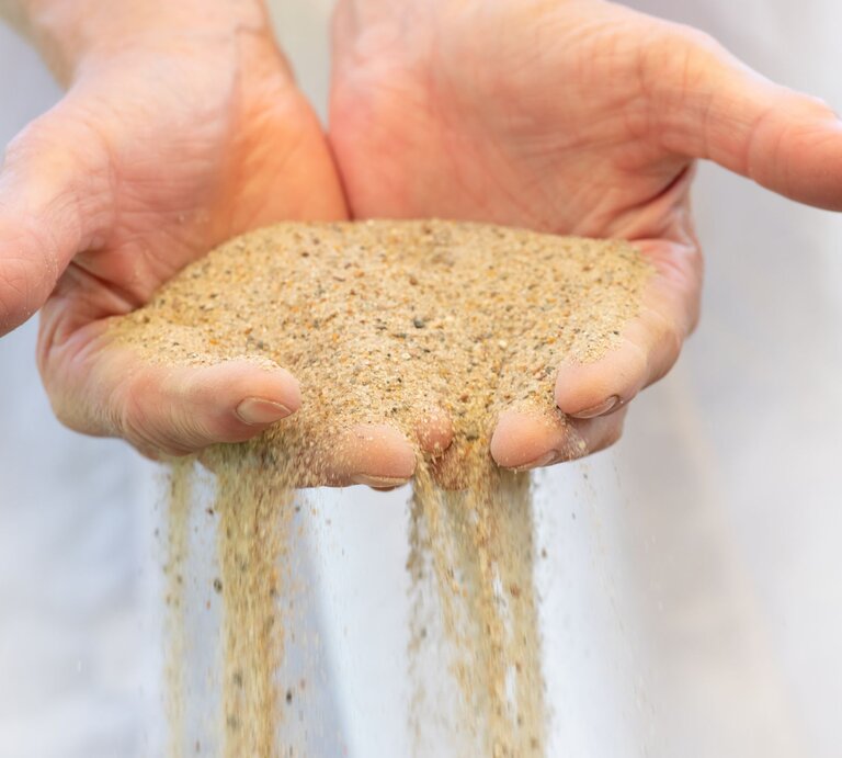 Zwei offene Hände lassen feinen, goldbraunen Sand langsam zwischen den Fingern hindurchrieseln. | © Adobe Stock/Rainer Fuhrmann