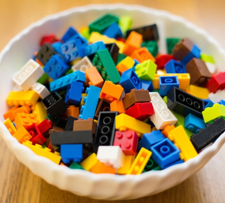 Eine weiße Schale voller bunter Legosteine in verschiedenen Formen und Farben steht auf einem Holztisch. | © Adobe Stock/Zsolt Biczó