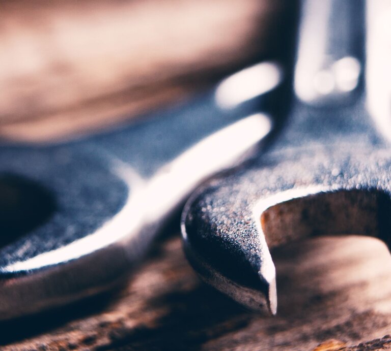 Nahaufnahme von zwei metallischen Schraubenschlüsseln, die auf einem rustikalen Holzuntergrund liegen. | © Adobe Stock/S...