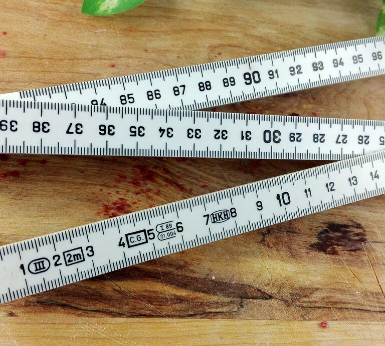 Ein Zollstock mit Zentimeter-Skalierung liegt auf einem Holztisch. | © Adobe Stock/Manuela Manay
