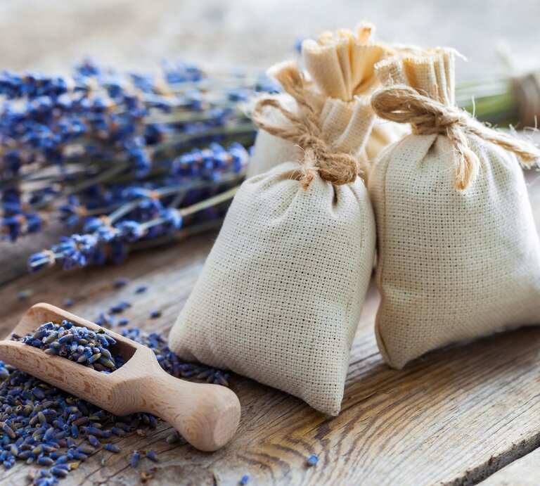 Drei mit Kordel verschlossene Duftsäckchen und ein Holzlöffel liegen auf einem hölzernen Tisch neben Lavendel. | © Getty Images/ChamilleWhite