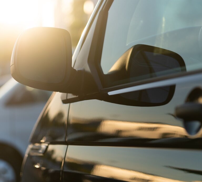 Ein parkendes schwarzes Auto, dessen Seitenspiegel von der untergehenden Sonne angestrahlt wird, daneben ein weißes Fahrzeug. | © Getty Images/deepblue4you