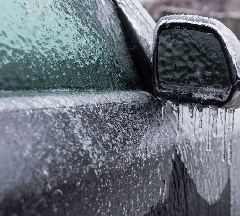 Außenspiegel und Fenster eines Autos komplett von einer dicken Eisschicht bedeckt, an der Eiszapfen hängen. | © Adobe Stock/danmir12