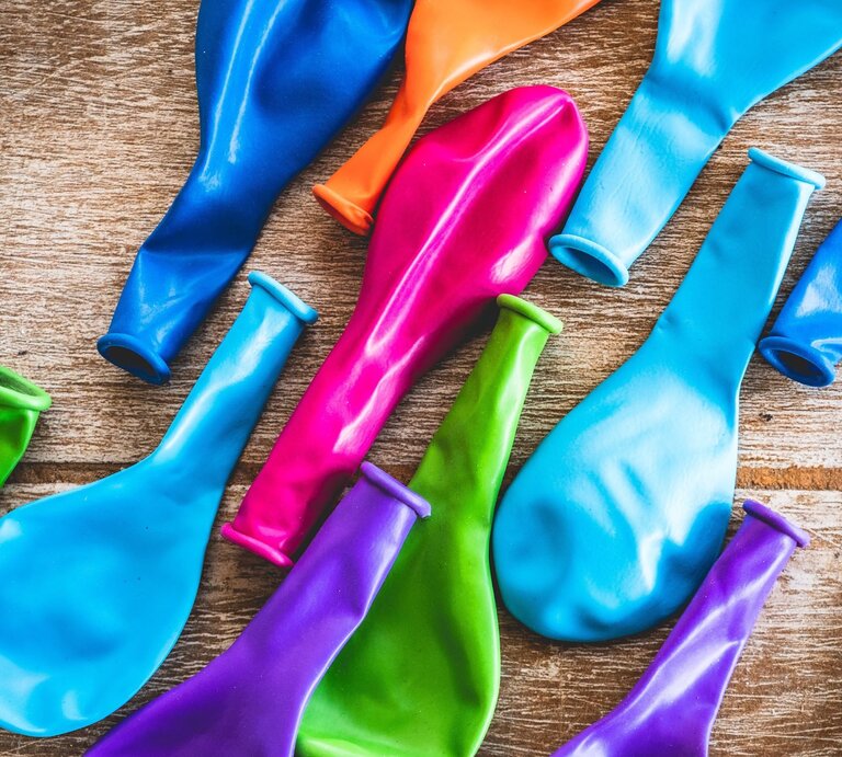 Bunte, unaufgeblasene Luftballons in verschiedenen Farben liegen verstreut auf hellem Holz. | © Getty Images