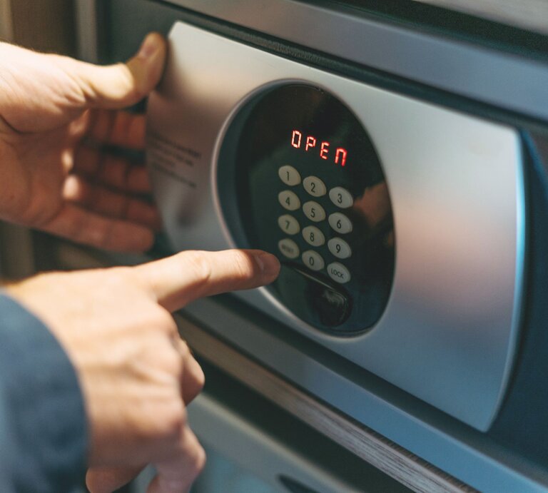Nahaufnahme von Händen, die einen geöffneten Safe durch Eingabe des Zahlencodes entriegeln. | © Adobe Stock/Galina Zhigalova