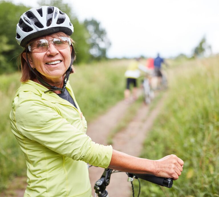 Ältere Frau auf dem Fahrrad trägt einen Fahrradhelm in der Natur. | © Adobe Stock/Robert Kneschke