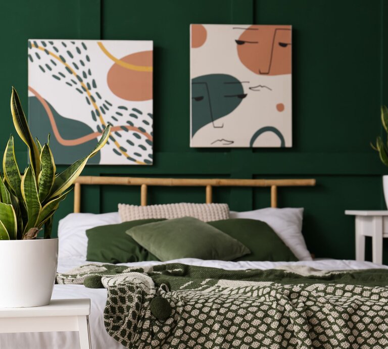 Modern eingerichtetes Schlafzimmer mit grünem Wandanstrich, Pflanzen in weißen Töpfen und abstrakter Kunst über dem Bett. | © Adobe Stock / Pixel-Shot