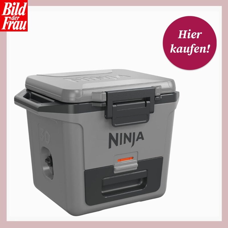 Graue Ninja-Kühlbox mit silbernem Deckel und schwarzen Verschlüssen vor hellem Hintergrund. Links oben ist das Logo von "Bild der Frau" zu sehen, rechts oben ein pinker Kreis mit der Aufschrift "Hier kaufen!". Die Kühlbox steht leicht schräg und zeigt das Ninja-Logo auf der Vorderseite. | © Amazon/Canva/Collage:bildderfrau.de