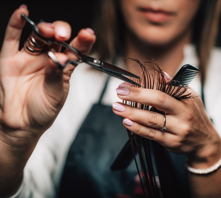 Nahaufnahme von Händen einer Friseurin mit Schere und Kamm beim präzisen Schneiden brauner Haare. Trendfrisuren 2025 | © Adobe Stock/ Microgen