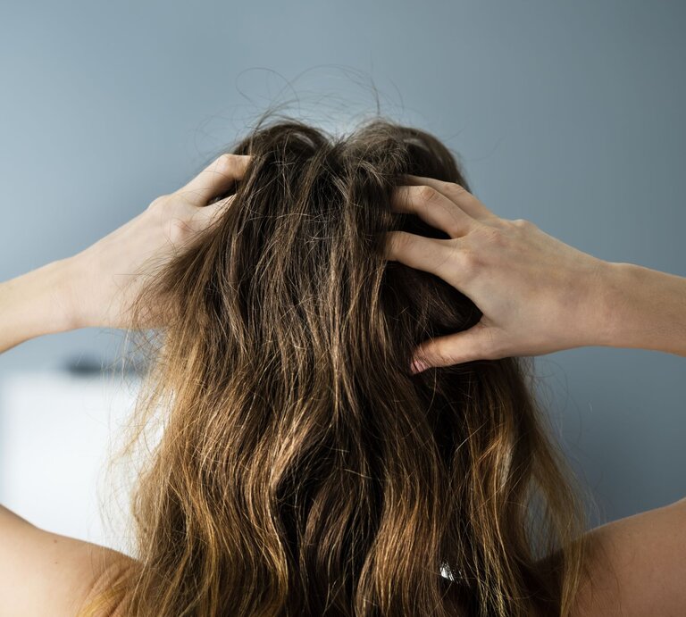 Frau von hinten mit verwuscheltem braunem Haar fasst sich mit den Händen in die Haare. | © Adobe Stock/ Andrey Popov