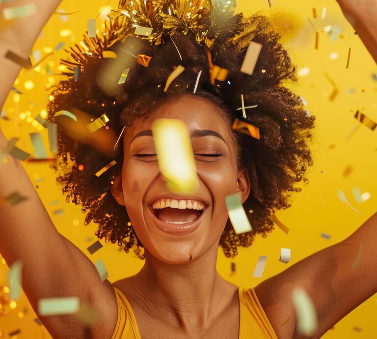Junge Frau mit lockigem Haar lacht ausgelassen unter goldenem Lametta vor einem leuchtend gelben Hintergrund. | © AdobeStock/NooPaew (Generiert mit KI)