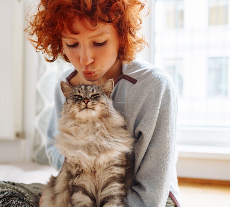 Rothaarige Frau gibt Katze einen Kuss | © Getty Images
