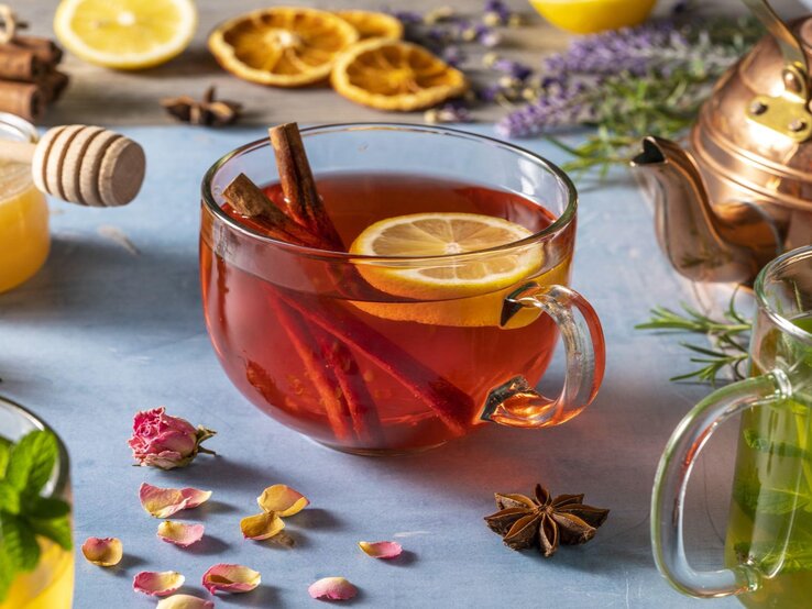 Detox-Tee zum Abnehmen Ein Glas Tee umgeben von Kräutern und gesunden Zusätzen, wie einer Zitrone.