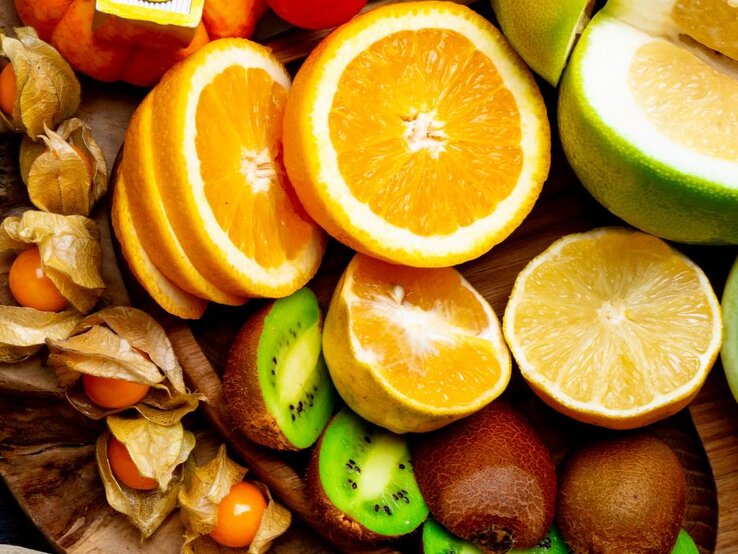 Aufgeschnittene Orangen, Grapefruit, Kiwi und Physalis liegen nebeneinander auf einem Holzuntergrund und zeigen eine Auswahl vitamin-C-reicher Früchte.