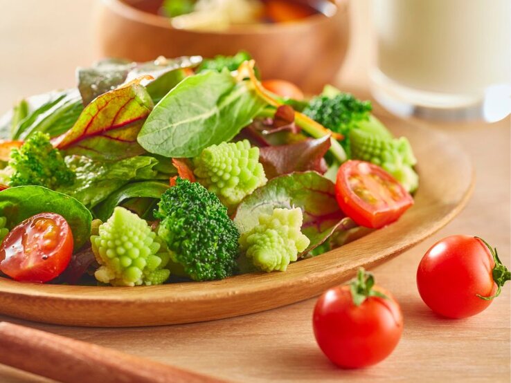 Bunter Teller mit Tomaten, Brokkoli und Spinat und Mangold darauf. 