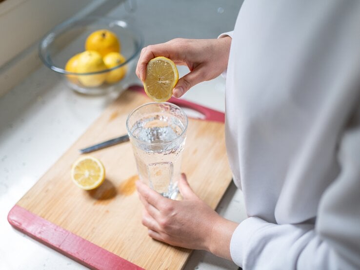 Die Knoblauch-Zitronen-Kur stärkt dein Immunsystem und senkt den Blutdruck. Eine Frau presst den Saft einer halben Zitrone in ein Glas.