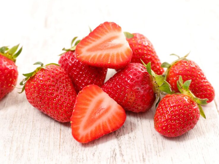 Reife Erdbeeren, teilweise aufgeschnitten, auf hellem Holztisch – süße Vitamin-C-Quelle für gesunde Haut und starke Abwehrkräfte. | © Getty Images Pro/ margouillatphotos via Canva.com