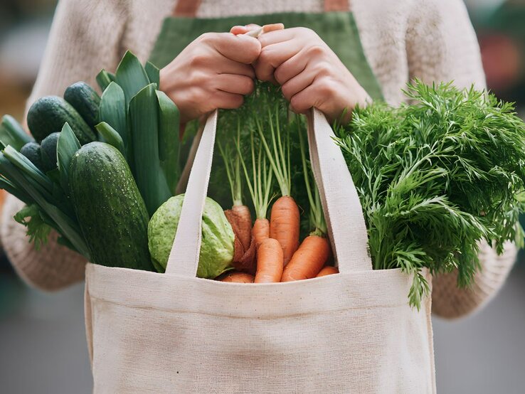 Eine Frau hält ein Einkaufsnetz mit gesundem Gemüse, das beim Abnehmen helfen soll.
