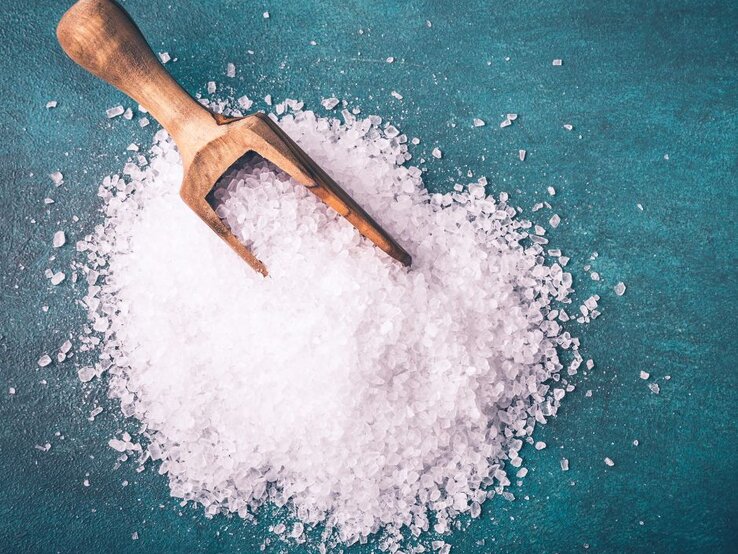 Ein Holzlöffel liegt auf grobem Meersalz, das auf einer grünlichen Unterlage verstreut ist.
