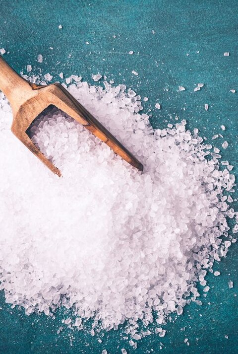 Ein Holzlöffel liegt auf grobem Meersalz, das auf einer grünlichen Unterlage verstreut ist.