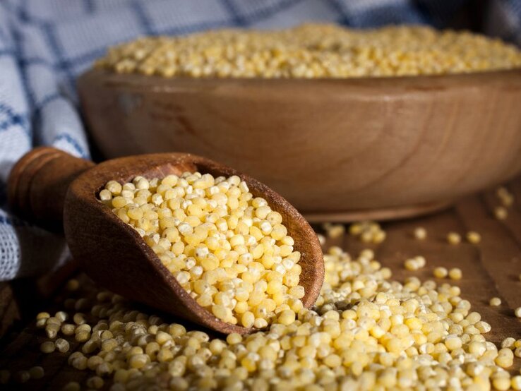 Holzschaufel mit gelber Hirse, dahinter eine Schale voller Körner. | © Getty Images/ NikiLitov via Canva.com